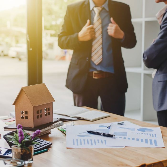 Two people talking in the background with a table with a small house, flowers, and paperwork